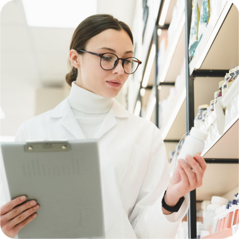 Pharmacist holding a prescription bottle in one hand and a clipboard in the other to fulfill a patient’s order.